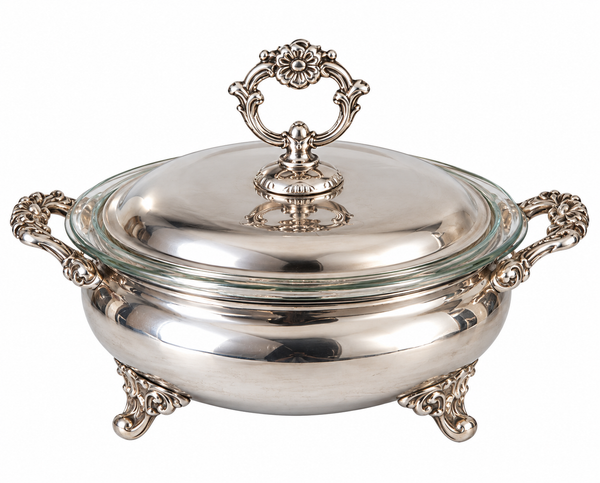 A polished silver chafing dish with a glass lid, ornate silver handles, and decorative feet, shown on a white background.