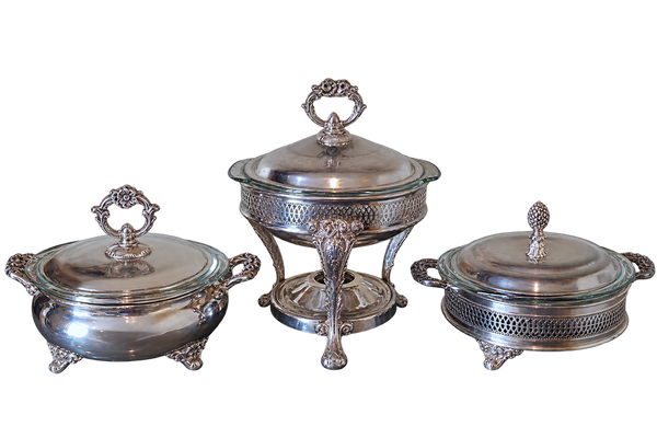 Three-piece silver chafing dinner set with matching lids, including a central pedestal chafier and two side bowls with ornate handles and feet, isolated on a white background.