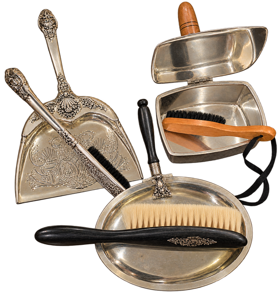 A vintage set of silver-colored metal cleaning and grooming tools, including an ornate dustpan with a brush, a small metal washbasin with a brush inside, and a metal tray with a grooming brush, all arranged on a white background.